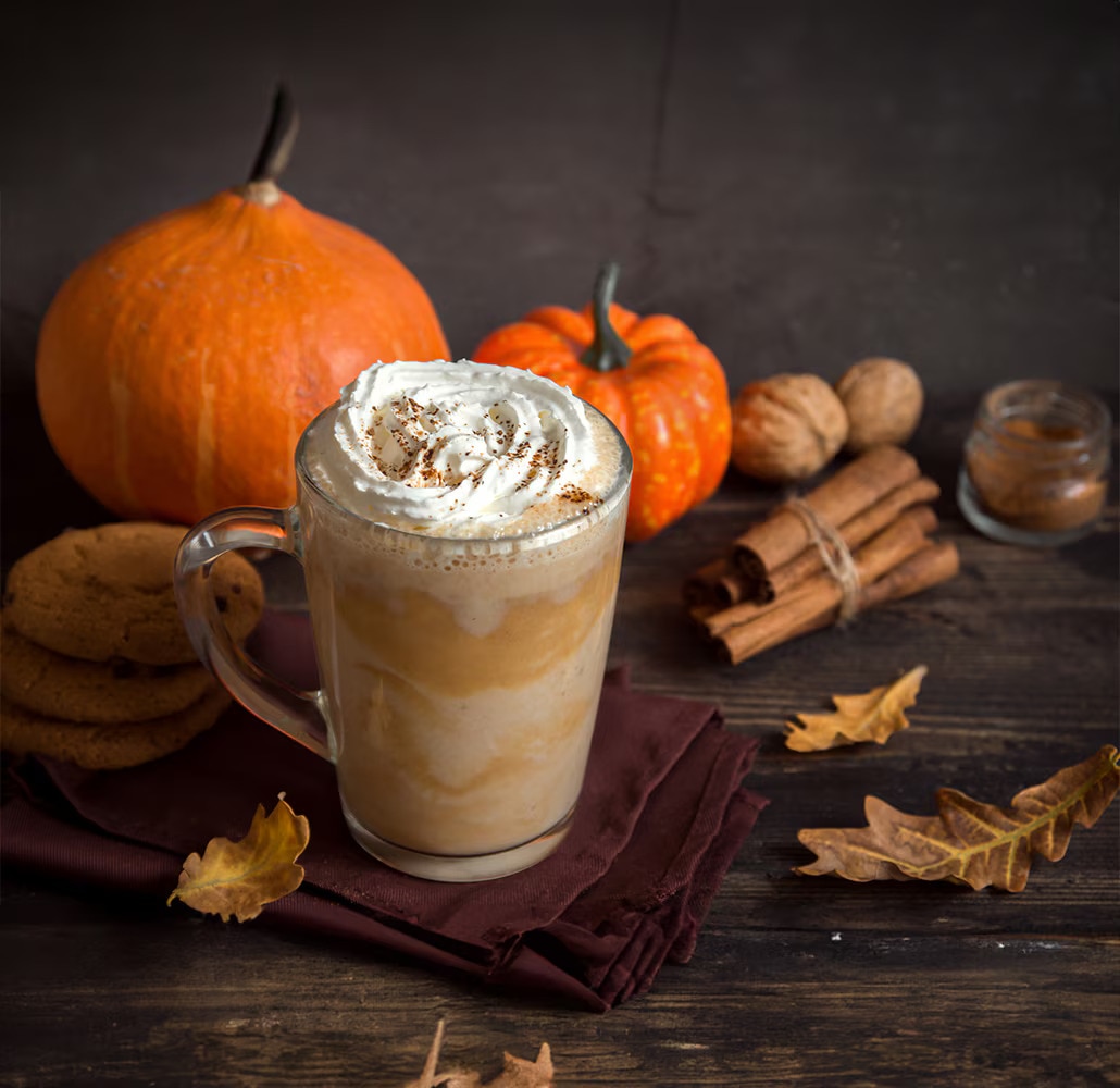 Pumpkin spice latte met slagroom, omringd door pompoenen.