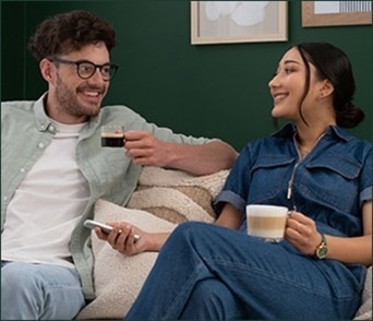 Een glimlachend koppel ontspant op de bank en geniet van NESCAFÉ Dolce Gusto koffie